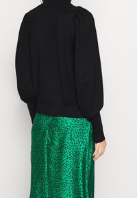 Maglione nero lavorato a maglia con maniche a sbuffo, abbinato a una gonna di satin verde con un motivo astratto nero. Orlo e polsini a costine.