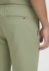 Lysgrønne bukser lavet af et struktureret stof, med en elastisk talje, en baglomme med en dekorativ stribet detalje.