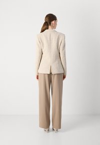 Beige tweed-loosukko, jossa on muotoiltu design, takana venttiili, yhdistettynä beigeihin leveisiin housuihin ja kärkiin korkokenkiin.