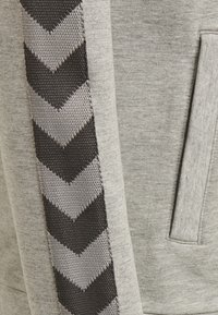 Grå hoodie med en chevronmönstrad rand i svart och ljusgrå längs sidan. Mjuk textur, med en känguruficka fram.