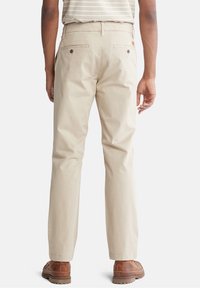 Beiga bomullshoser med rak bendesign, två bakfickor med knappstängning och en subtil textur. Bärs med bruna skor.