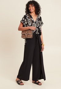 Zwart-wit gestreepte blouse, ruime zwarte broek, bruine schoudertas met een sluiting, en zwarte sandalen met een kurken zool.