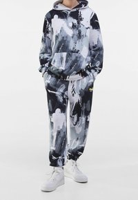 Felpa con cappuccio e pantaloni coordinati in un motivo astratto a schizzi di vernice nero, bianco e grigio, realizzati in tessuto morbido, abbinati a scarpe da ginnastica bianche.