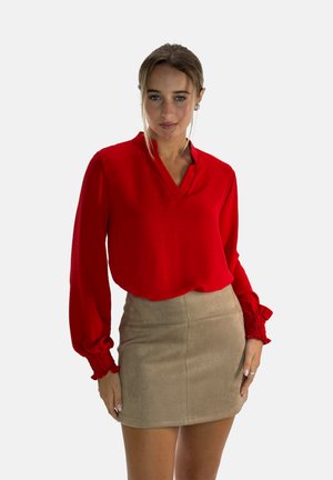Rode blouse met lange mouwen en een V-hals, gecombineerd met een beige suède miniskirt. Soepele textuur met subtiele ontwerpelementen.