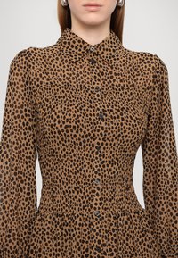 Abito camicia marrone con stampa leopardata nera, dotato di colletto, apertura frontale con bottoni e vita arricciata. Maniche lunghe con una sottile texture.