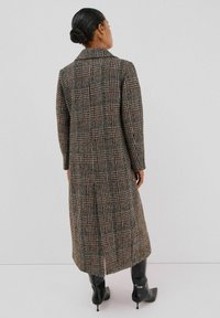 Lange geblokte jas in bruin, zwart en teal; voorzien van een gelapte kraag, lange mouwen en een rechte snit, die tot halverwege de kuit reikt, met een gestructureerde afwerking.