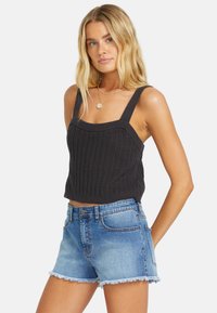 Tummanharmaa neulottu crop-top, jossa on tekstuurinen kuosi ja leveät olkaimet, yhdistettynä vaaleansinisiin farkkushortseihin, joissa on risat reunat.