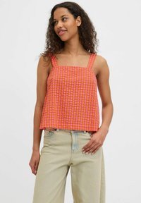 Top senza maniche a quadri arancioni e rosa con scollatura quadrata e spalline larghe, abbinato a jeans chiari e dal fit rilassato.