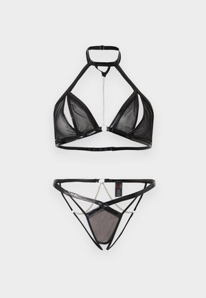 Juodas permatomas tinklelio apatinio trikotažo rinkinys su halterio kaklo liemenėle, trikampio formos kaušeliais ir derančiomis juostelėmis puoštomis grandinėlių detalėmis ant balto fono.