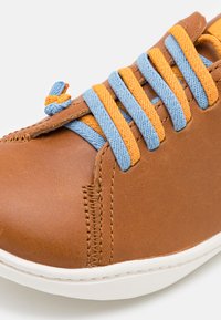 Scarpa in pelle marrone con lacci in tessuto blu e arancione. Punta arrotondata, suola bianca a contrasto e dettagli cuciti lungo il lato.