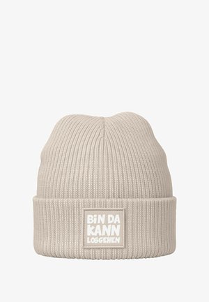 Beige knit beanie with a textured ribbed design. Features a folded cuff and a rectangular patch with white lettering.