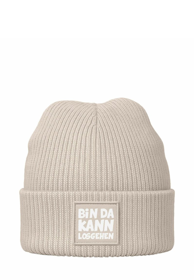 Beige knit beanie with a textured ribbed design. Features a folded cuff and a rectangular patch with white lettering.