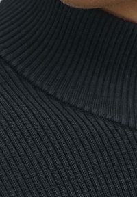 Lähikuva mustast ribbeeritud kaeluskleidist inimese ülemisel rinnal ja kaelal.