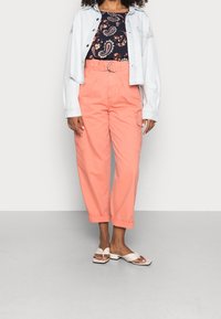 Růžové cargo kalhoty s vysokým pasem a ohrnutými manžetami, doplněné tmavě květinovým topem a světle modrou džínovou bundou. Bílými plochými sandály je look dokončen.