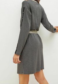 Robe grise avec de longues manches et des accents noirs, ceinture texturée dorée, au design décontracté. Tissu doux avec un style décontracté.