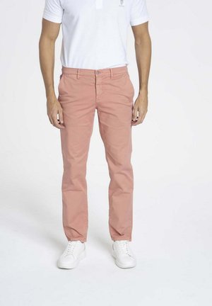 Chinos en coton rose pour homme, coupe slim, avec poches avant et fermeture éclair, associés à des baskets blanches et un polo blanc.