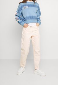 Světle modrá mikina s batikováním, na které je nápis "HELLO KITTY" a grafika na rukávech, v kombinaci se světle růžovými rovnými kalhotami a bílými teniskami.