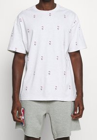 Szary bawełniany t-shirt z wzorem logo NBA na całej powierzchni, w małych, kolorowych nadrukach. Posiada okrągły dekolt i luźny krój.