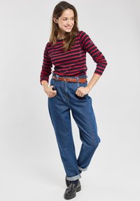 Rood en marineblauw gestreepte blouse met lange mouwen, gedragen met blauwe high-waisted denimbroek, geaccentueerd met een bruine leren riem, en zwarte loafers.