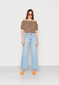 Top floral off-the-shoulder em preto com flores amarelas, rosas e laranjas. Calças largas de cintura alta em azul claro e sandálias laranjas.