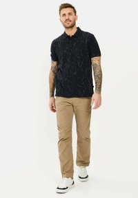 Marineblauwe polo met korte mouwen en een gestructureerd bladdessin, gecombineerd met beige chinos en witte sneakers met zwarte accenten. Casual fit.
