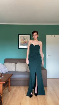 Žalia nesandari suknelė su širdelės iškirpte, šonu plyšiu ir susiraukšlėjimu. Ji turi karoliukų dirželius ir tekstūruotą audinį. Juodi aukštakulniai.