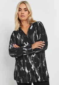 Button-up blouse in black and white abstract pattern, featuring long sleeves, a collar, and a textured fabric with side slits.