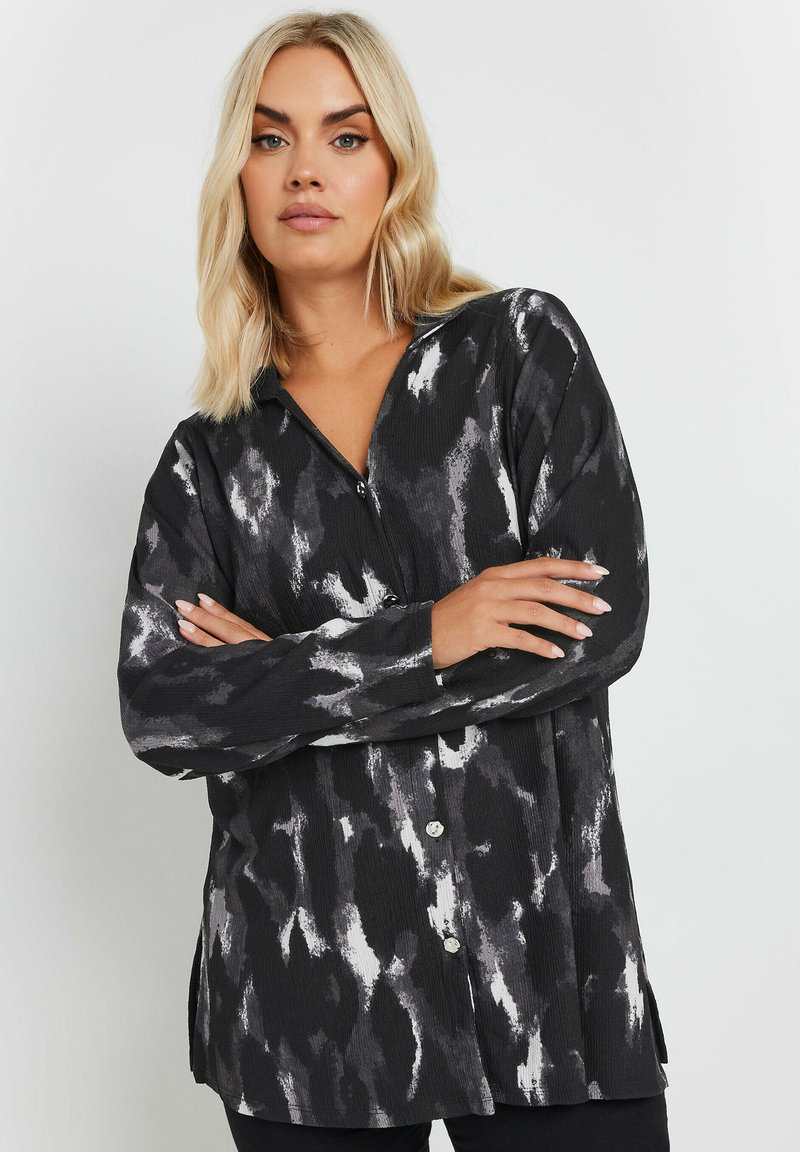 Button-up blouse in black and white abstract pattern, featuring long sleeves, a collar, and a textured fabric with side slits.
