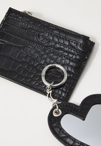  tarjetero negro de cuero sintético con textura de cocodrilo, accesorio de llavero plateado y detalle de espejo en forma de corazón. Acentos en hardware plateado.