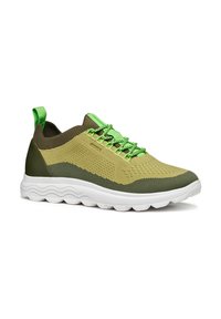 Zapatilla verde y beige con parte superior de punto transpirable, patrón texturizado y suela blanca flexible. Presenta cordones verdes y una lengüeta en la parte trasera.
