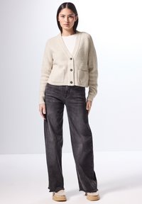 Beige ribbad stickad cardigan med sjalkrage, fem svarta knappar och framfickor, tillsammans med löst sittande urblekta svarta jeans och beigea skor.