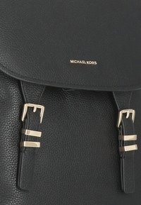 Zaino in pelle nera con texture, dotato di due cinturini con fibbie dorate e logo "MICHAEL KORS" in lettere dorate sulla patta.