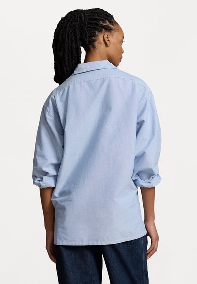 Light blue button-up shirt with rolled sleeves, made of soft cotton. Features a pointed collar and a relaxed fit. Back view shows stitching details.