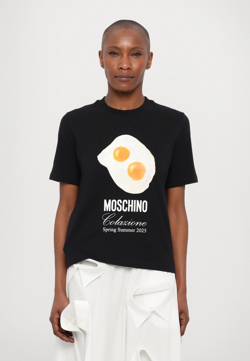 Zwarte katoenen t-shirt met een afbeelding van twee gebakken eieren, met daaronder in het wit gedrukt "Moschino Colazione Lente Zomer 2025".