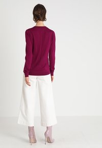 Magenta långärmad topp med en figurnära silhuett, matchad med vida vita byxor. Modellen bär ljusrosa högklackade anklarstövlar.