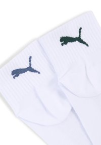 Para białych skarpet z prążkowaną teksturą, z ciemnozielonym i granatowym logo Pumy na mankietach. Klasyczny design sportowy.