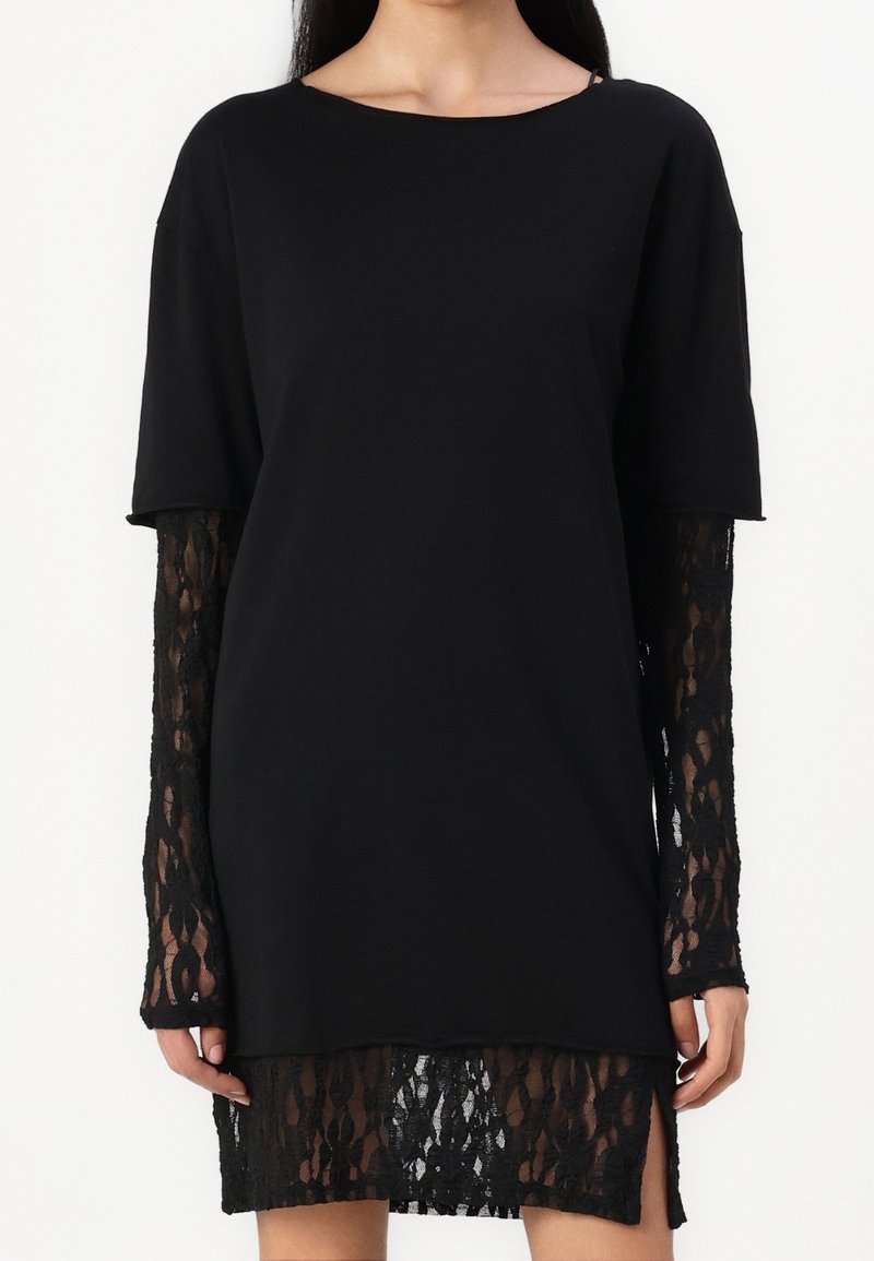 Zwarte top met korte mouwen en lange kantmouwen; de kanten zoom onthult een patroon. Zacht materiaal, relaxte pasvorm met zijsplitten.