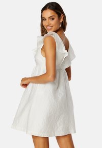 Bíl dress s texturou, s volánkovými ramínky, přiléhavým korzetem a rozšířenou sukní, se zapínáním na zip na zadní straně.