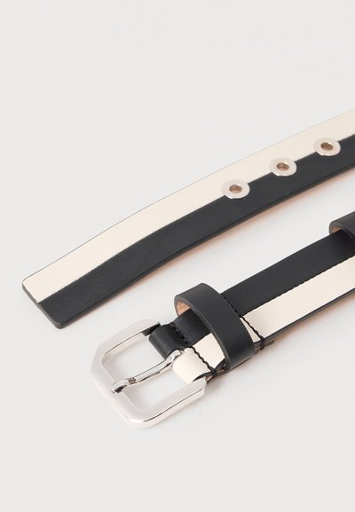 Μαύρη και λευκή δερμάτινη ζώνη με ασημένια πόρπη και τέσσερις μεταλλικές οπές σε ανοιχτό φόντο.