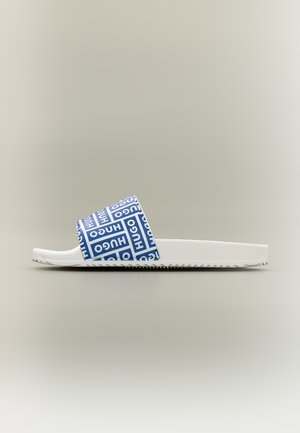 Bílá nazouvací pantofle se modrým páskem s opakujícím se nápisem „HUGO“ v bílých blokových písmenech, zobrazená z profilu na jednobarevném pozadí.