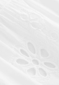 Tissu blanc présentant une broderie florale élaborée. Le matériau est léger avec une texture lisse, mettant en valeur des motifs découpés décoratifs.