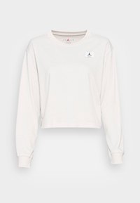 Cropped long-sleeve shirt in light beige cotton with a crew neckline and a small black Jordan logo patch on the left chest.