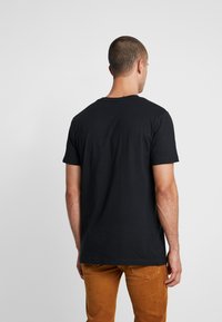 Zwart T-shirt met korte mouwen van katoen, met een ronde hals en een ontspannen pasvorm. Achteraan is de gladde textuur en het eenvoudige ontwerp zichtbaar.