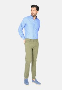 Camicia a quadri blu chiaro, pantaloni verde oliva e scarpe slip-on blu. Design slim fit con colletto button-down e motivi sottili sulla camicia.