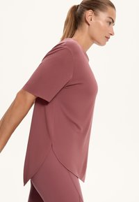 Ružová športová blúzka s krátkymi rukávmi, vo voľnom strihu a zakriveným spodným okrajom. Vyrobená z hladkej, elastickej tkaniny.