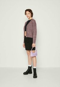 Knitted burgundy cardigan with buttons, black crop top, black mini skirt, and chunky black boots. Holding a small textured lilac bag.