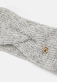 Fascetta grigia lavorata a maglia con design intrecciato, realizzata in morbida lana. Presenta un piccolo logo in metallo dorato.