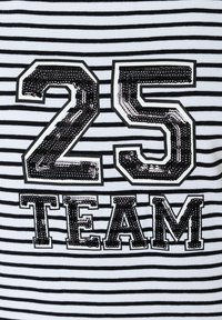 Schwarz-weißer Streifenstoff zeigt die Zahl "25" und "TEAM" in fetten, paillettenbesetzten schwarzen Zahlen mit glänzendem Finish.