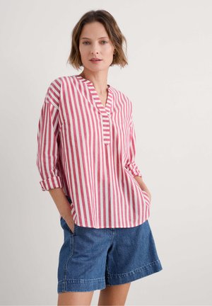 Chemise légère à rayures rouges et blanches, avec un col et un léger décolleté en V, à manches retroussées, accompagnée d'un short en denim.