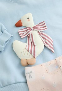 Hellblaues Sweatshirt mit einer plüschigen Entenapplikation und einer gestreiften Schleife. Die Ente hat einen weißen Körper, einen orangefarbenen Schnabel und beige Füße. In der Nähe befindet sich ein pinkfarbener Stoff mit Mustern.